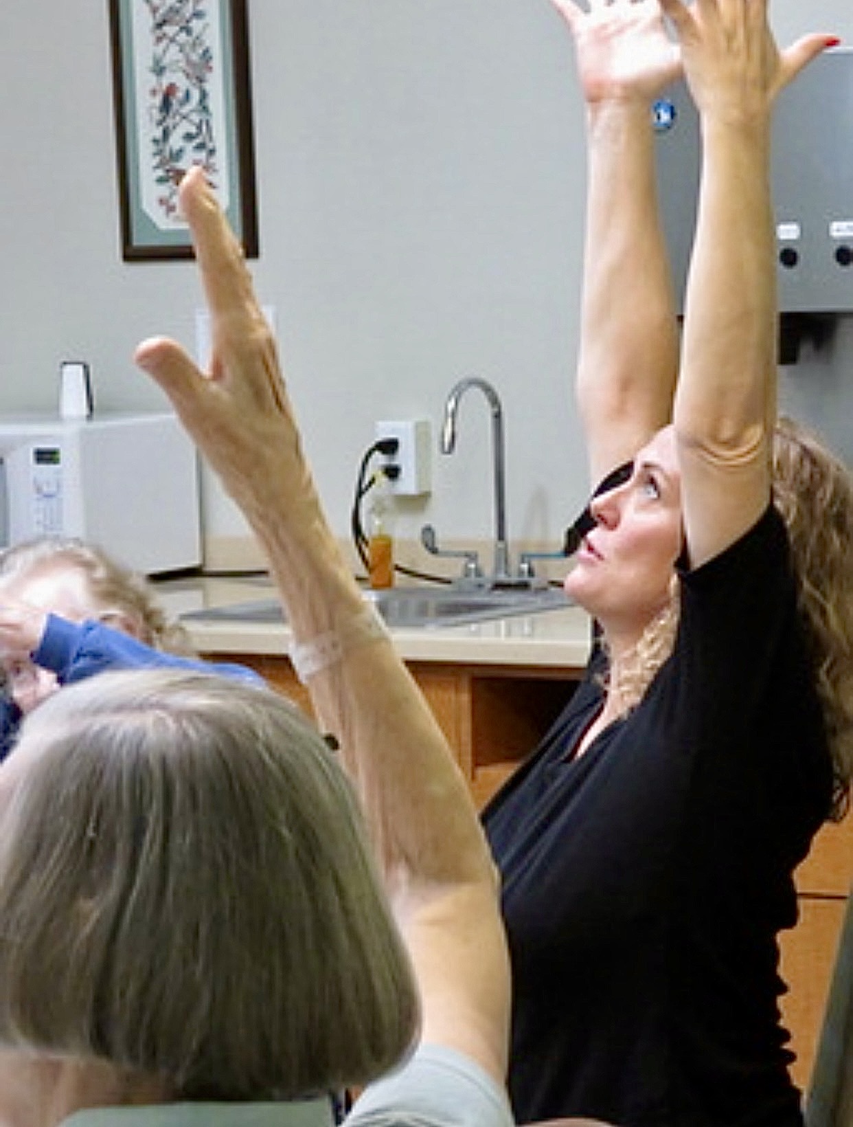 Close up of VictoriAnn guiding a seated stretch, arms raised